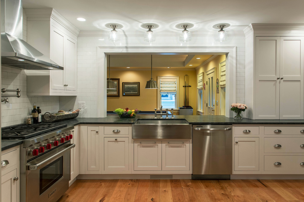 This is an example of a mid-sized transitional l-shaped eat-in kitchen in Boston with a farmhouse sink, white cabinets, granite benchtops, white splashback, stainless steel appliances, medium hardwood floors, no island, shaker cabinets and ceramic splashback.