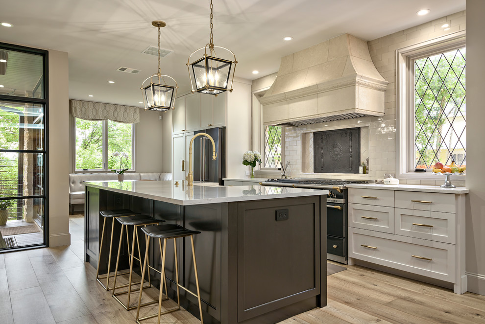 This is an example of a mid-sized transitional galley open plan kitchen in Austin with black cabinets, quartz benchtops, porcelain splashback, black appliances, light hardwood floors, with island, white benchtop, a farmhouse sink, shaker cabinets, beige splashback and beige floor.