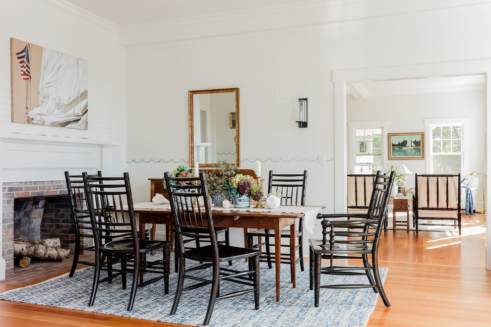 Inspiration for a beach style dining room in Boston with white walls, medium hardwood floors, a standard fireplace, a brick fireplace surround and orange floor.