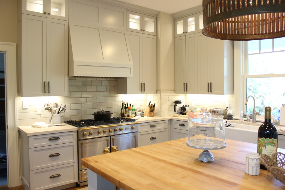 Photo of a large country u-shaped eat-in kitchen in San Francisco with a farmhouse sink, beaded inset cabinets, white cabinets, granite benchtops, white splashback, subway tile splashback, stainless steel appliances, light hardwood floors and multiple islands.