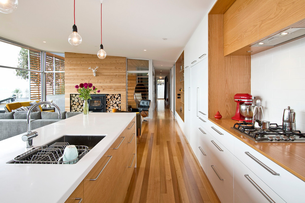 Inspiration for a large contemporary single-wall open plan kitchen in Hobart with an undermount sink, flat-panel cabinets, white cabinets, solid surface benchtops, white splashback, stainless steel appliances, light hardwood floors and with island.