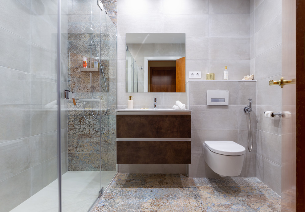 Inspiration for a small contemporary master bathroom in Barcelona with flat-panel cabinets, brown cabinets, an alcove shower, a wall-mount toilet, white tile, ceramic tile, beige walls, ceramic floors, a trough sink, multi-coloured floor, a hinged shower door and white benchtops.