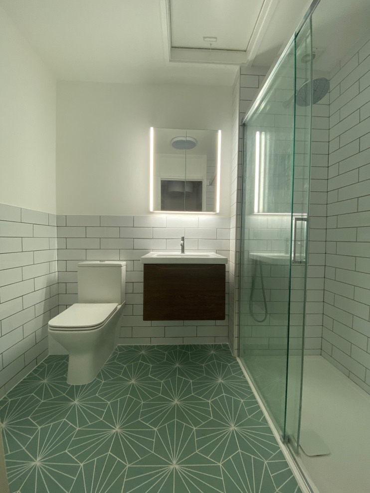 Foto på ett mellanstort funkis vit badrum för barn, med släta luckor, bruna skåp, en dusch i en alkov, en toalettstol med hel cisternkåpa, vit kakel, porslinskakel, vita väggar, klinkergolv i keramik, ett väggmonterat handfat, laminatbänkskiva, grönt golv och dusch med skjutdörr