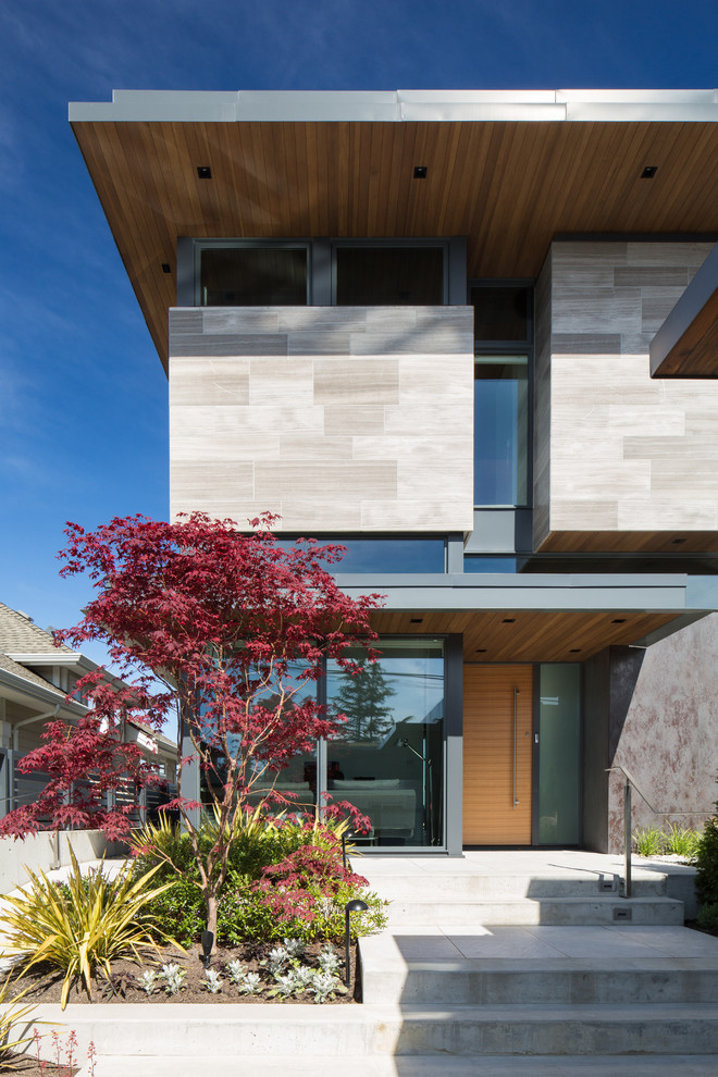 This is an example of a small two-storey grey exterior in Vancouver with stone veneer and a flat roof.