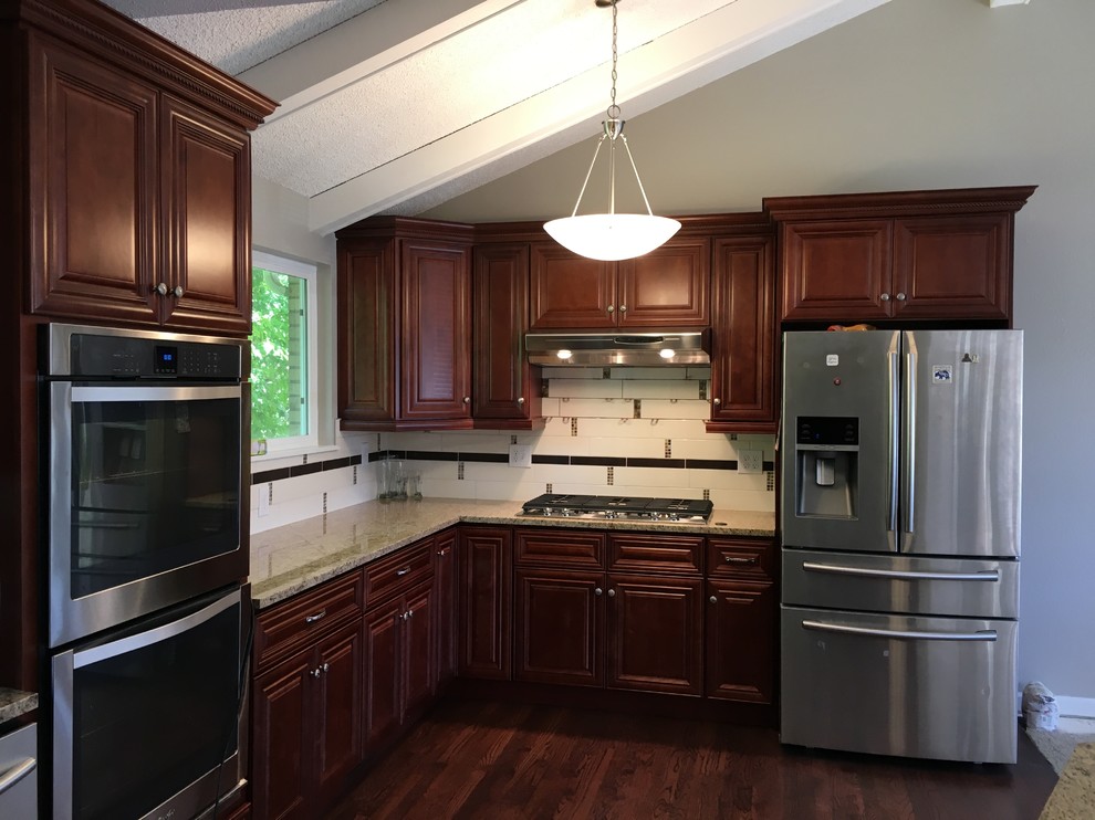 Open concept kitchen - mid-sized transitional l-shaped laminate floor and brown floor open concept kitchen idea in Denver with an undermount sink, raised-panel cabinets, dark wood cabinets, granite countertops, multicolored backsplash, ceramic backsplash, stainless steel appliances and an island