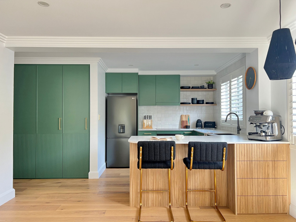 Medium sized contemporary u-shaped open plan kitchen in Sydney with a submerged sink, recessed-panel cabinets, green cabinets, engineered stone countertops, yellow splashback, porcelain splashback, black appliances, medium hardwood flooring, a breakfast bar, brown floors and white worktops.
