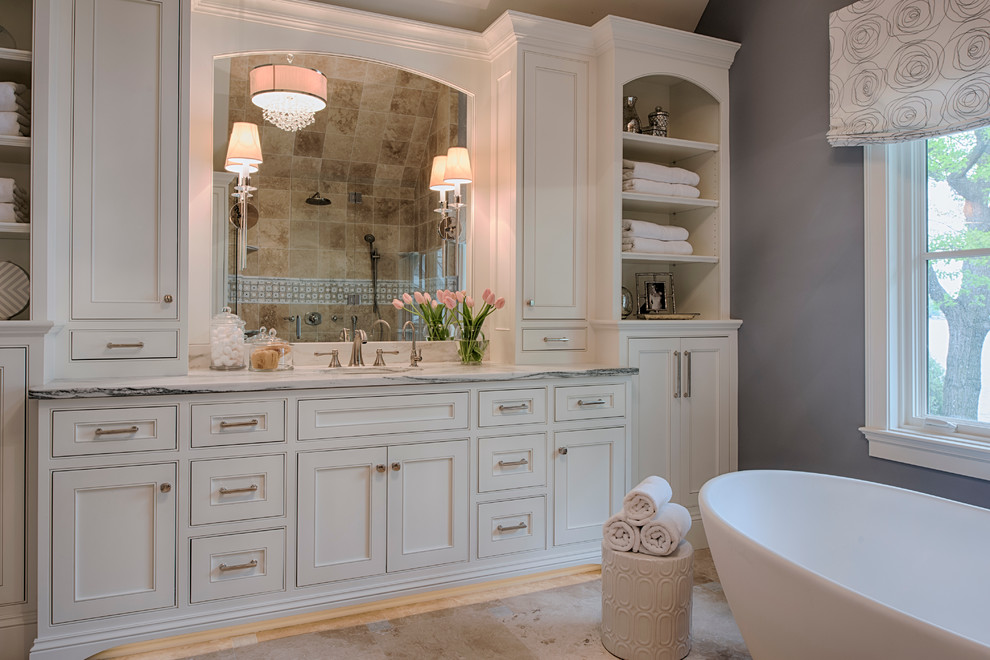 Design ideas for a mid-sized transitional 3/4 bathroom in Minneapolis with recessed-panel cabinets, white cabinets, a freestanding tub, beige tile, ceramic tile, grey walls, limestone floors, an undermount sink and beige floor.