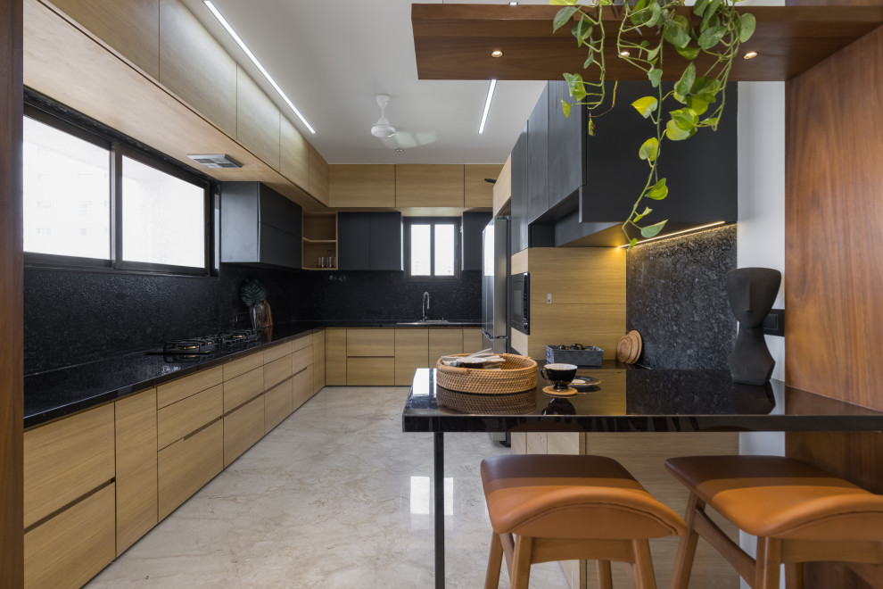 This is an example of a large contemporary u-shaped eat-in kitchen with a triple-bowl sink, flat-panel cabinets, beige cabinets, granite benchtops, black splashback, granite splashback, stainless steel appliances, marble floors, no island, beige floor and black benchtop.