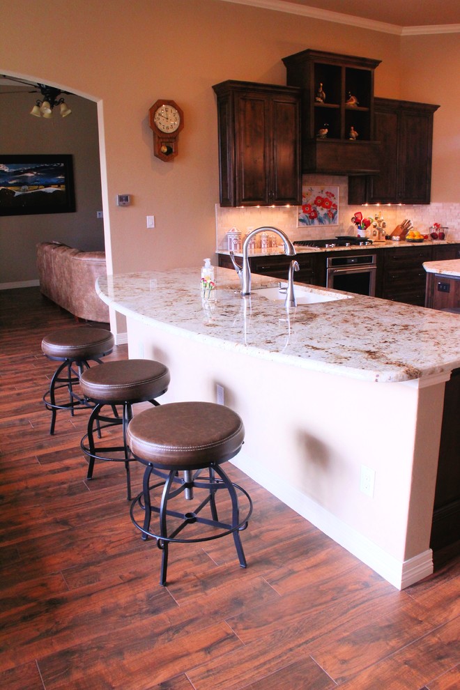 Enclosed kitchen - mid-sized rustic u-shaped dark wood floor and brown floor enclosed kitchen idea in Austin with an island, an undermount sink, raised-panel cabinets, dark wood cabinets, granite countertops, beige backsplash, stone tile backsplash and stainless steel appliances