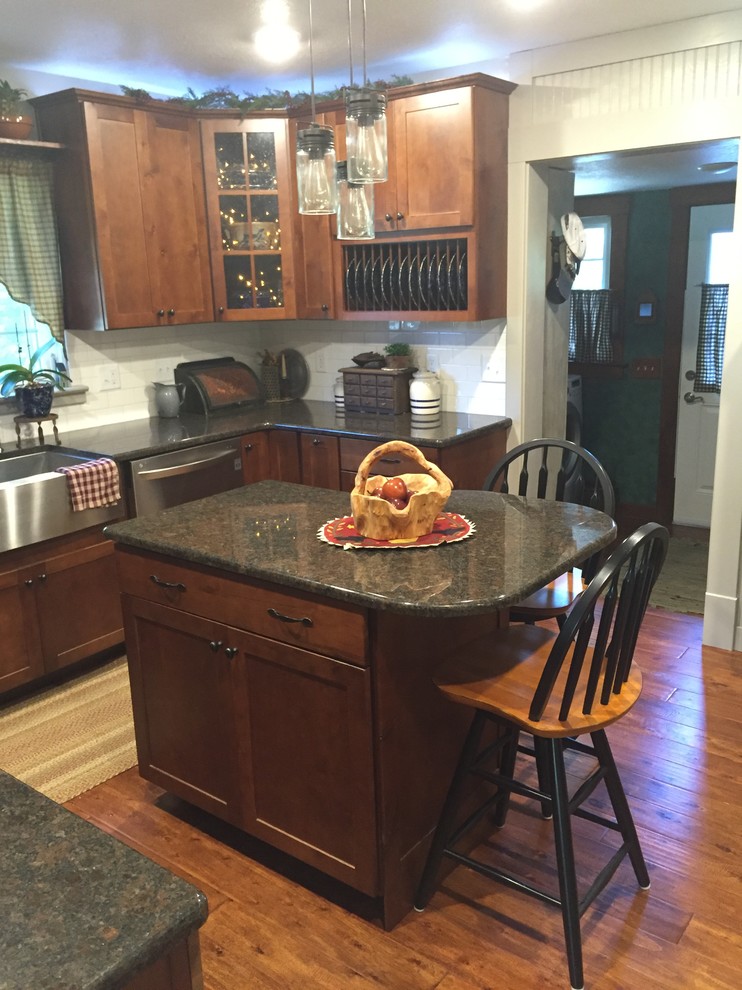 Example of a mid-sized transitional u-shaped enclosed kitchen design with a farmhouse sink, shaker cabinets, medium tone wood cabinets, granite countertops, white backsplash, stainless steel appliances and an island