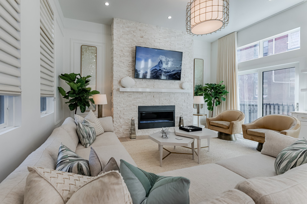 This is an example of a classic open plan living room in Philadelphia with white walls, light hardwood flooring, a standard fireplace, a stacked stone fireplace surround, a wall mounted tv and wainscoting.