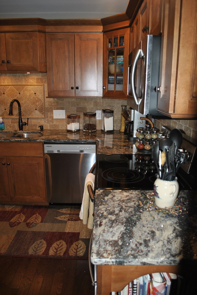 Brown floor kitchen photo with brown cabinets, beige backsplash, stainless steel appliances, an island and gray countertops