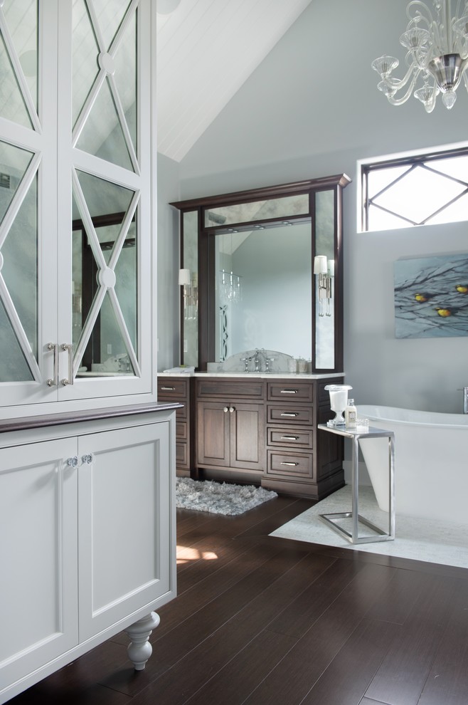 This is an example of an expansive transitional bathroom in Kansas City with an undermount sink, recessed-panel cabinets, dark wood cabinets, marble benchtops, a freestanding tub, a two-piece toilet, white tile, stone slab, grey walls and bamboo floors.