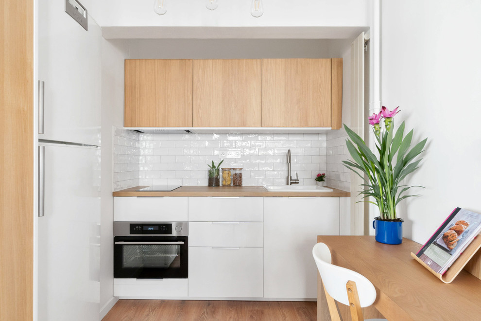 Contemporary l-shaped open plan kitchen in Paris with a drop-in sink, flat-panel cabinets, white cabinets, wood benchtops, white splashback, subway tile splashback, panelled appliances, light hardwood floors and a peninsula.