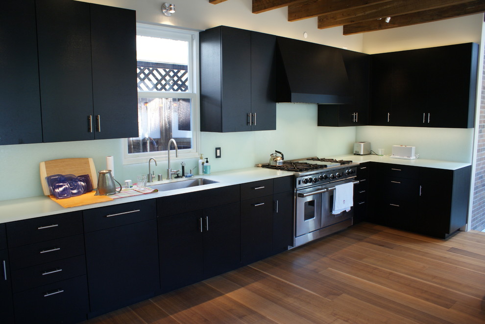 This is an example of a mid-sized modern l-shaped eat-in kitchen in Denver with an undermount sink, flat-panel cabinets, black cabinets, glass benchtops, white splashback, glass sheet splashback, stainless steel appliances, dark hardwood floors and no island.