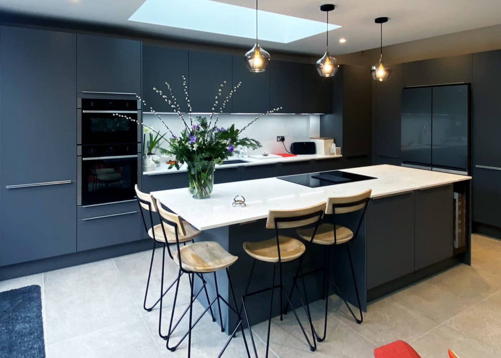 Inspiration for an expansive modern single-wall open plan kitchen in London with a single-bowl sink, flat-panel cabinets, grey cabinets, quartzite benchtops, white splashback, engineered quartz splashback, black appliances, porcelain floors, with island, white floor and white benchtop.