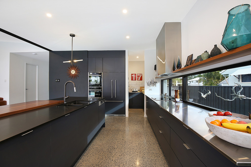 Design ideas for a mid-sized contemporary galley open plan kitchen in Sunshine Coast with an undermount sink, flat-panel cabinets, grey cabinets, granite benchtops, panelled appliances, concrete floors, with island, grey floor and black benchtop.