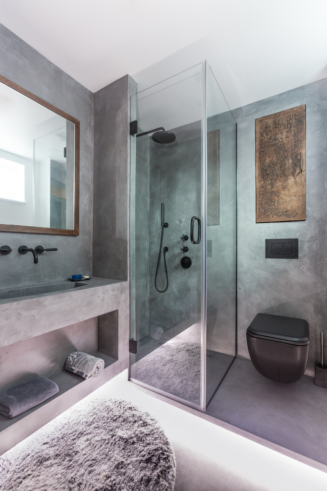 Photo of a small industrial 3/4 bathroom in London with a wall-mount toilet, gray tile, grey walls, concrete floors, grey floor, a hinged shower door, open cabinets, grey cabinets, a corner shower, an integrated sink, concrete benchtops and grey benchtops.