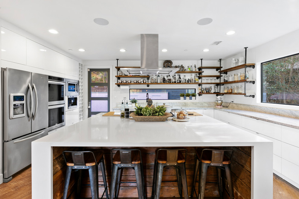 Urban u-shaped medium tone wood floor and brown floor kitchen photo in Los Angeles with flat-panel cabinets, white cabinets, stainless steel appliances, an island and gray countertops