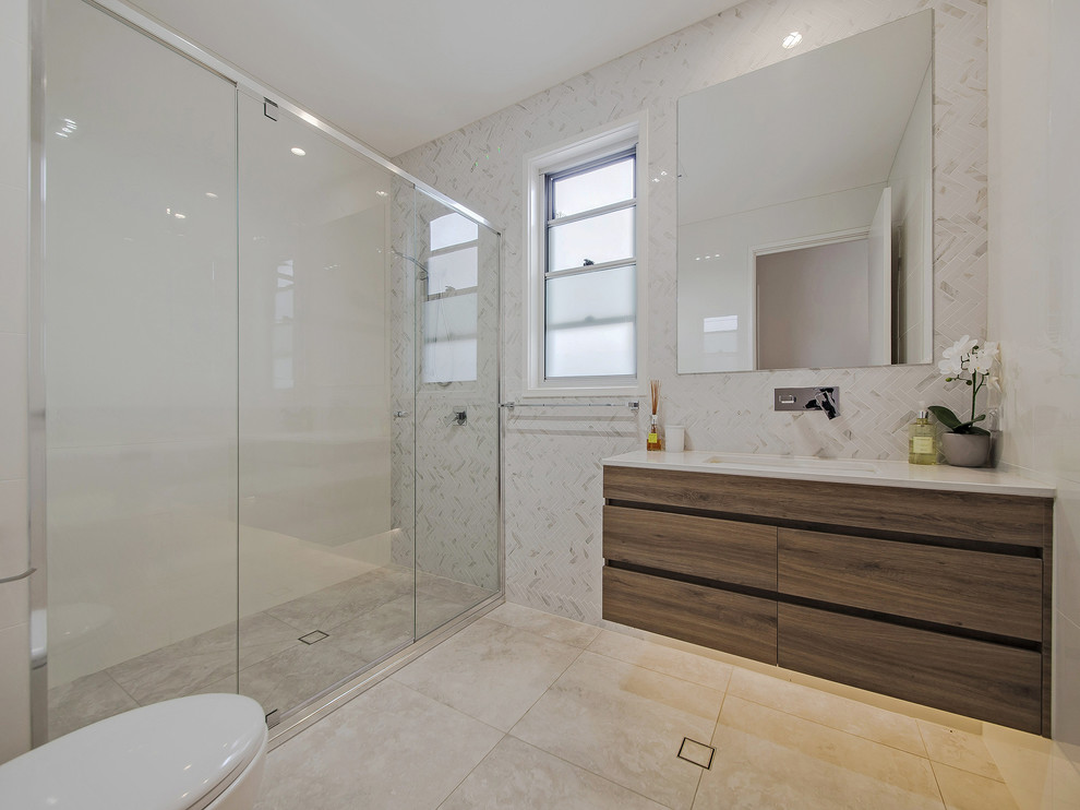 This is an example of a mid-sized contemporary kids bathroom in Brisbane with flat-panel cabinets, dark wood cabinets, a double shower, white tile, marble, white walls, an undermount sink, granite benchtops, beige floor and a hinged shower door.