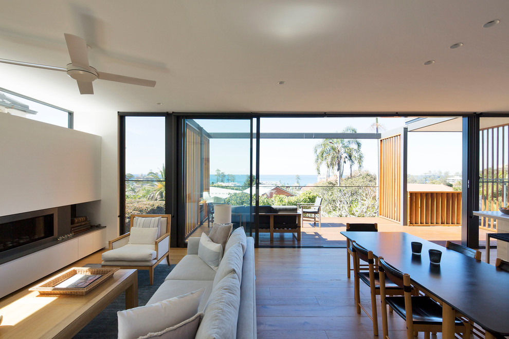 This is an example of a large contemporary open concept living room in Sydney with white walls, medium hardwood floors and a standard fireplace.