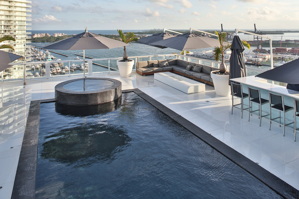 Design ideas for a mid-sized contemporary rooftop rectangular infinity pool in Miami with concrete slab and a hot tub.