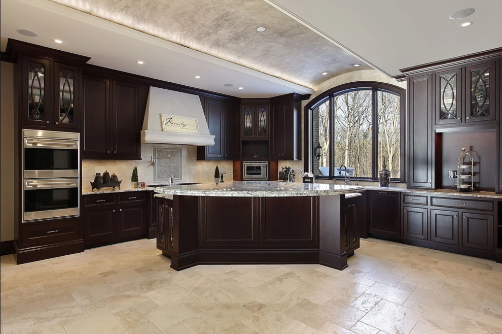 Large traditional l-shaped open plan kitchen in Los Angeles with an undermount sink, dark wood cabinets, granite benchtops, beige splashback, stainless steel appliances, with island, beige floor, recessed-panel cabinets, travertine floors and multi-coloured benchtop.