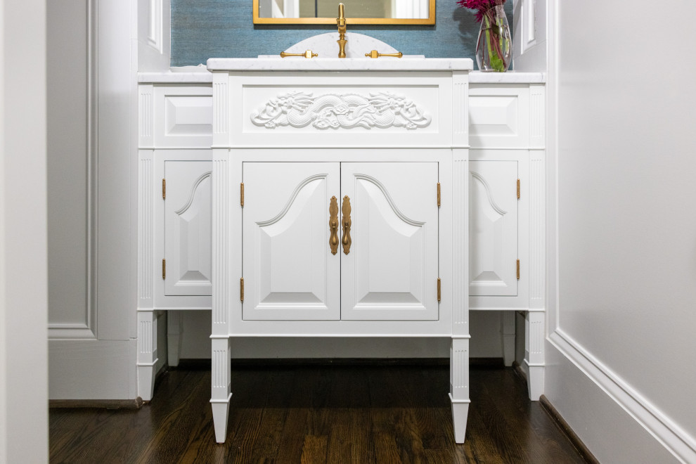 Inspiration for a mid-sized transitional powder room in Richmond with raised-panel cabinets, white cabinets, blue walls, medium hardwood floors, a console sink, marble benchtops, white benchtops, a freestanding vanity and wallpaper.