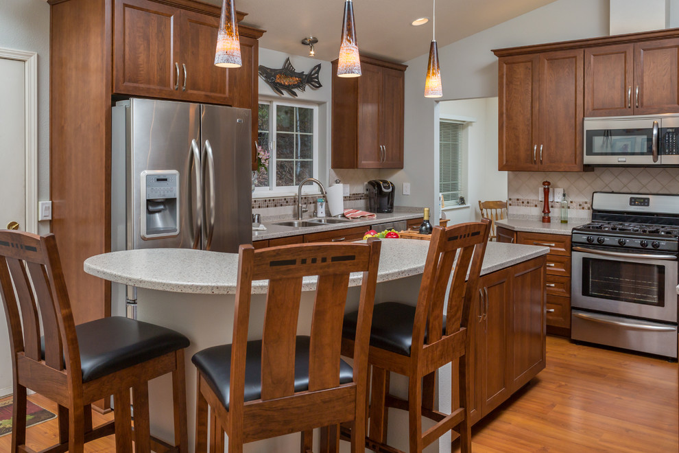 Mid-sized transitional u-shaped medium tone wood floor kitchen pantry photo with an undermount sink, recessed-panel cabinets, medium tone wood cabinets, solid surface countertops, beige backsplash, mosaic tile backsplash, stainless steel appliances and an island