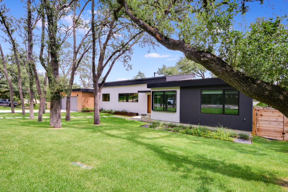 Inspiration for a mid-sized midcentury one-storey multi-coloured house exterior in Austin with mixed siding, a flat roof, a black roof and board and batten siding.