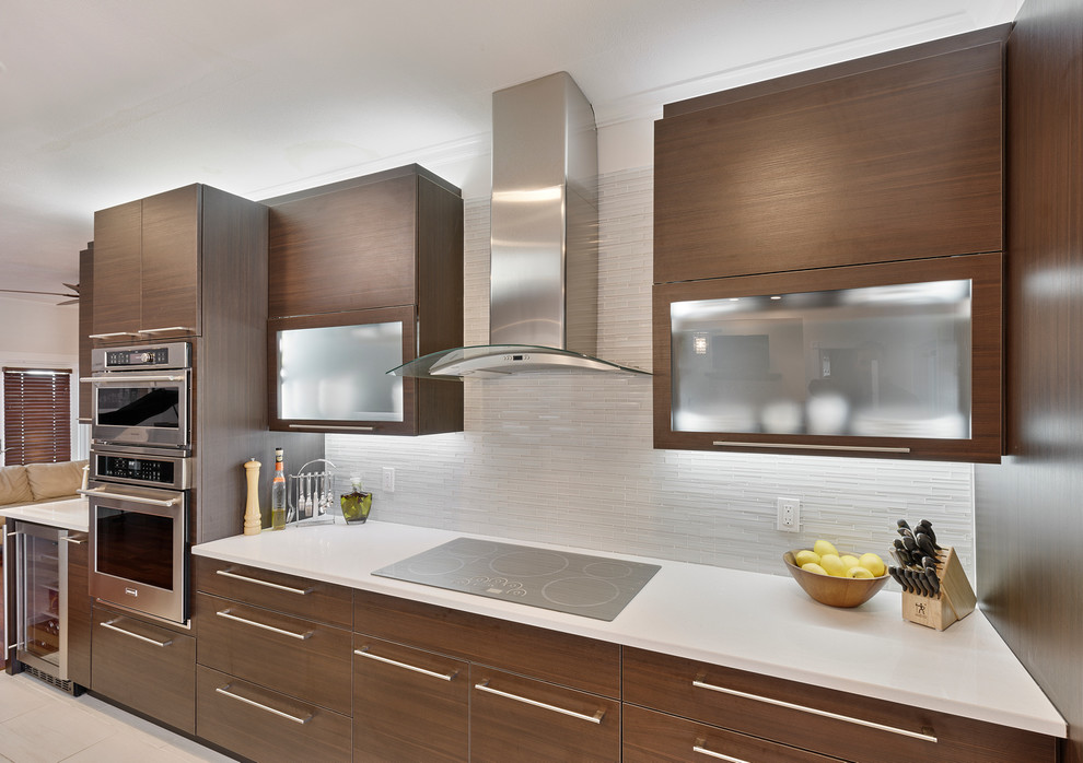 Example of a mid-sized minimalist l-shaped porcelain tile enclosed kitchen design in Miami with a double-bowl sink, flat-panel cabinets, dark wood cabinets, solid surface countertops, white backsplash, glass tile backsplash, stainless steel appliances and a peninsula