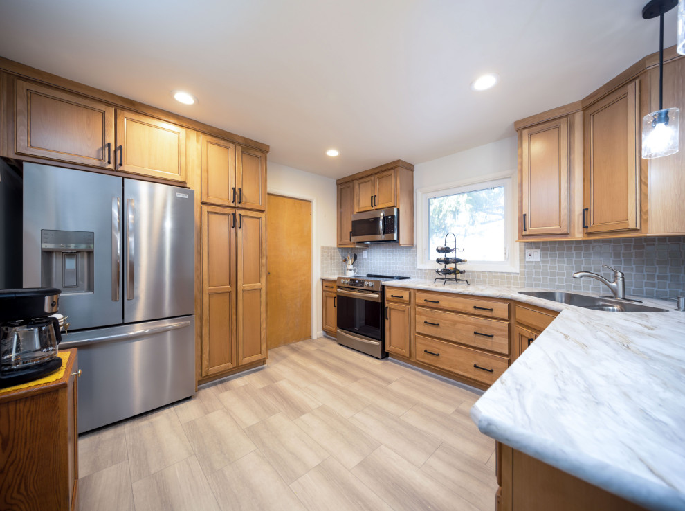 Mid-sized transitional l-shaped light wood floor and gray floor eat-in kitchen photo with an integrated sink, recessed-panel cabinets, light wood cabinets, laminate countertops, gray backsplash, porcelain backsplash, stainless steel appliances, a peninsula and white countertops