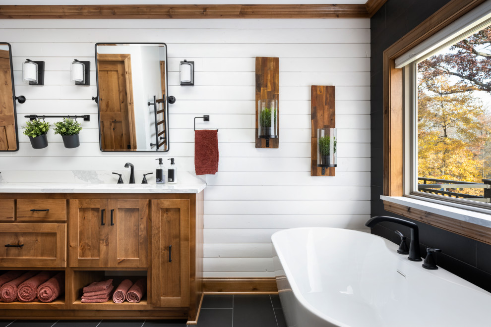 Example of a large farmhouse black tile and porcelain tile porcelain tile, black floor, double-sink and wall paneling freestanding bathtub design in Minneapolis with shaker cabinets, brown cabinets, an undermount sink, quartz countertops, white countertops and a built-in vanity