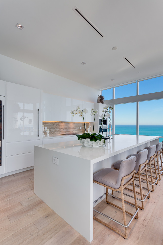 Mid-sized contemporary galley kitchen in Miami with an undermount sink, flat-panel cabinets, white cabinets, quartzite benchtops, beige splashback, ceramic splashback, light hardwood floors, with island, white benchtop, panelled appliances and beige floor.