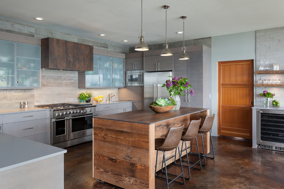 Inspiration for a mid-sized beach style u-shaped kitchen in Seattle with flat-panel cabinets, grey cabinets, ceramic splashback, stainless steel appliances, concrete floors, with island, brown floor, an undermount sink and beige splashback.