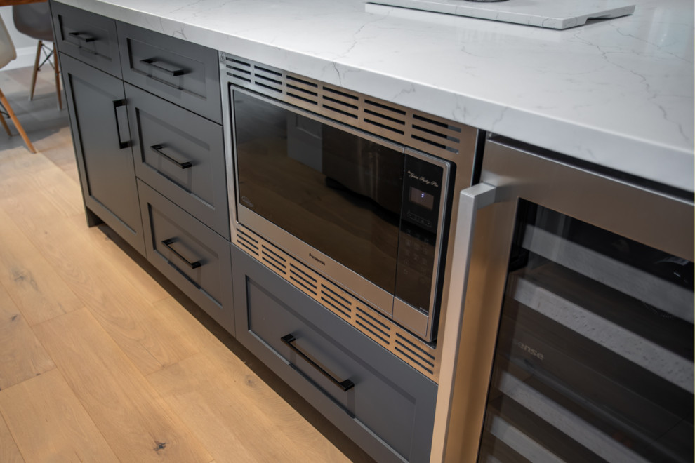 Example of a minimalist light wood floor and brown floor kitchen design in Toronto with shaker cabinets, blue cabinets, quartz countertops, stainless steel appliances, an island and white countertops