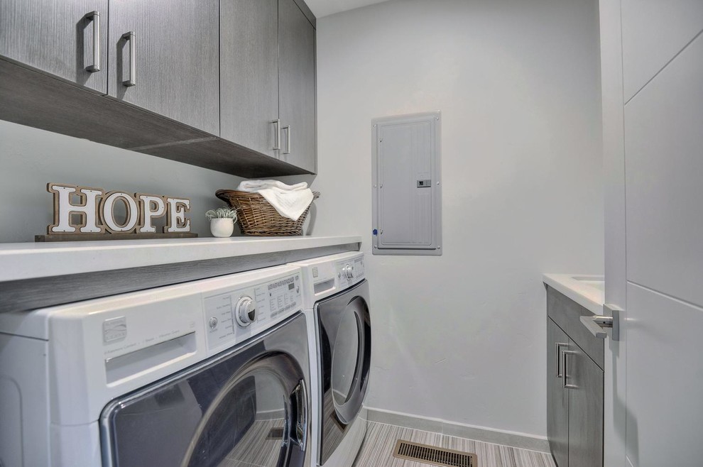 Photo of a small contemporary galley dedicated laundry room in San Francisco with a drop-in sink, flat-panel cabinets, distressed cabinets, concrete benchtops, grey walls, terra-cotta floors, a side-by-side washer and dryer, grey floor and white benchtop.