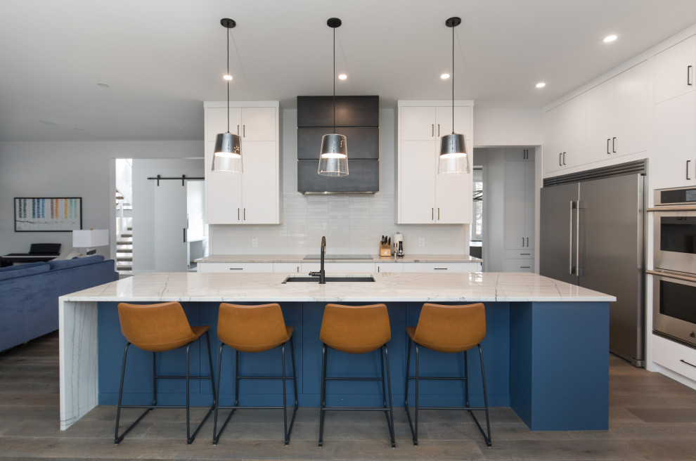 Large transitional l-shaped dark wood floor and gray floor kitchen pantry photo in Calgary with an undermount sink, flat-panel cabinets, white cabinets, quartzite countertops, white backsplash, matchstick tile backsplash, stainless steel appliances, an island and white countertops