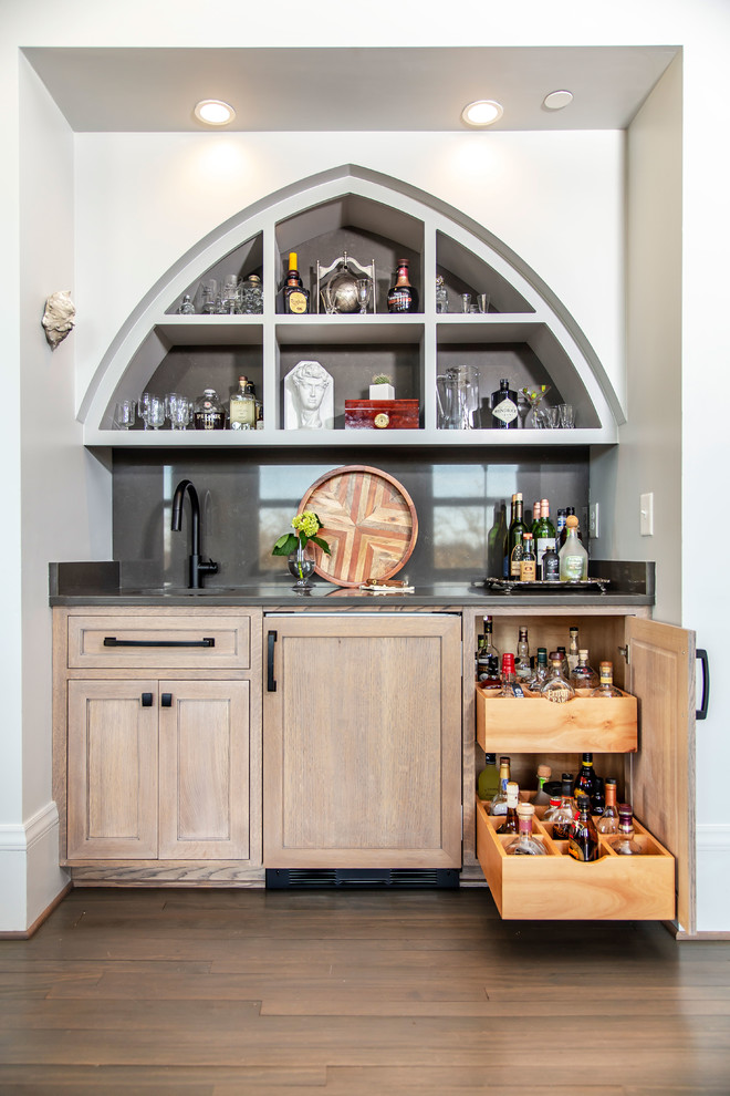 Example of a mid-sized transitional single-wall medium tone wood floor and brown floor wet bar design in Charlotte with an undermount sink, shaker cabinets, light wood cabinets, gray backsplash, stone slab backsplash and gray countertops