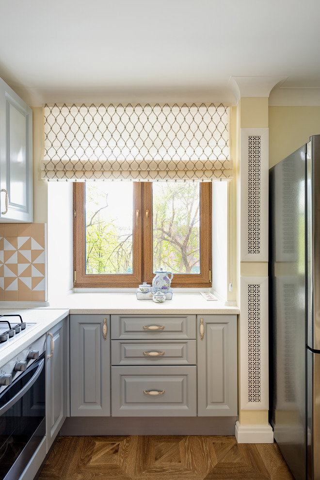 Exempel på ett litet kök, med luckor med infälld panel, grå skåp, laminatbänkskiva, beige stänkskydd, stänkskydd i keramik, rostfria vitvaror, laminatgolv och brunt golv