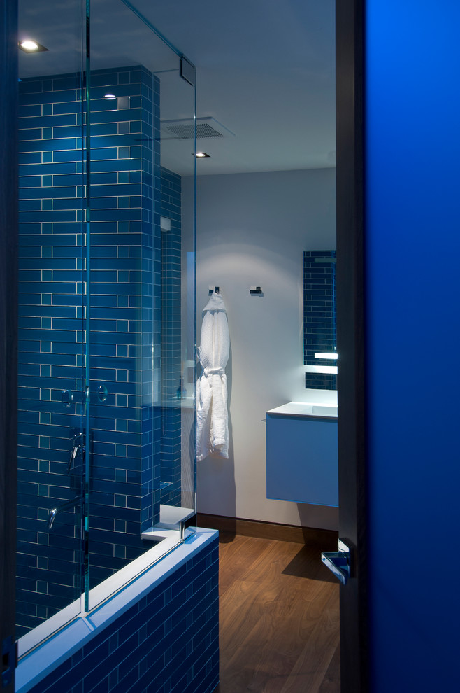 Mid-sized modern kids bathroom in Los Angeles with white cabinets, an alcove tub, a shower/bathtub combo, blue tile, blue walls, medium hardwood floors, an undermount sink, brown floor, a sliding shower screen, white benchtops, a single vanity, a floating vanity and recessed.