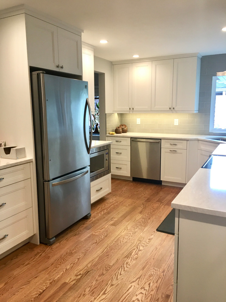Example of a small transitional u-shaped medium tone wood floor and brown floor enclosed kitchen design in Denver with a drop-in sink, shaker cabinets, white cabinets, quartz countertops, gray backsplash, subway tile backsplash, stainless steel appliances, a peninsula and white countertops