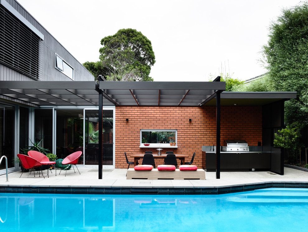 This is an example of a midcentury backyard patio in Melbourne with an outdoor kitchen, concrete pavers and a pergola.