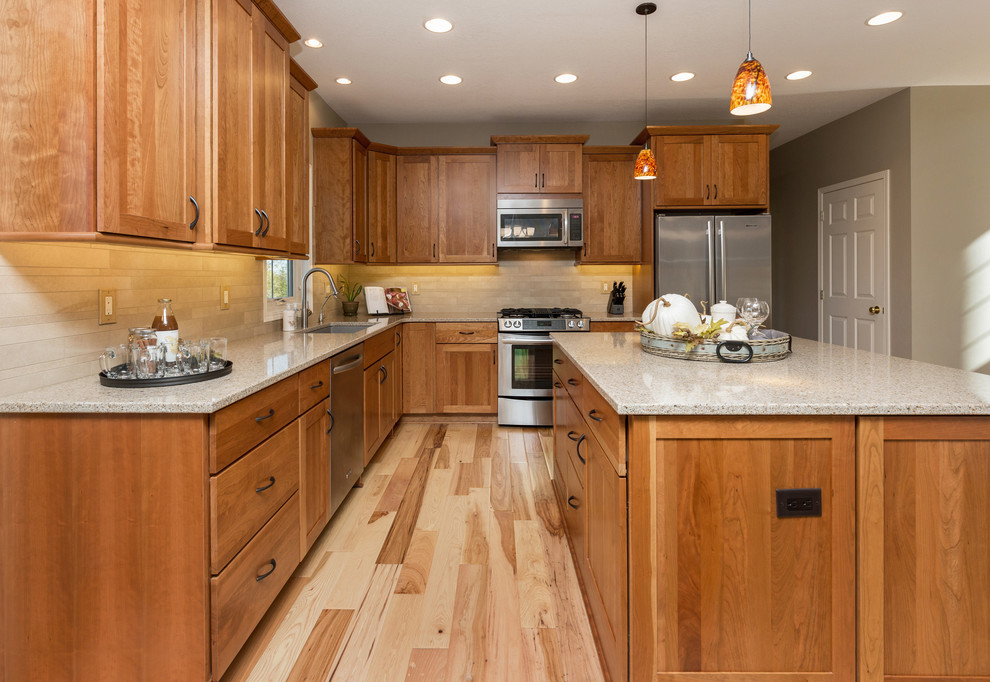 Example of a mid-sized transitional l-shaped light wood floor open concept kitchen design with an undermount sink, recessed-panel cabinets, medium tone wood cabinets, quartz countertops, beige backsplash, stone tile backsplash, stainless steel appliances and an island