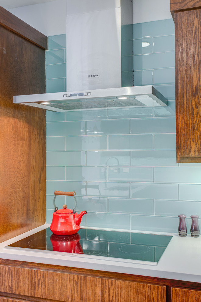 Photo of a mid-sized midcentury l-shaped eat-in kitchen in Dallas with an undermount sink, flat-panel cabinets, medium wood cabinets, quartz benchtops, blue splashback, glass tile splashback, stainless steel appliances, a peninsula and white benchtop.