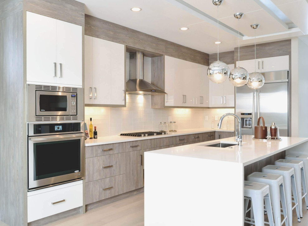 Large contemporary l-shaped eat-in kitchen in Calgary with an undermount sink, flat-panel cabinets, white cabinets, quartz benchtops, white splashback, glass tile splashback, stainless steel appliances, light hardwood floors, with island, beige floor, white benchtop and recessed.
