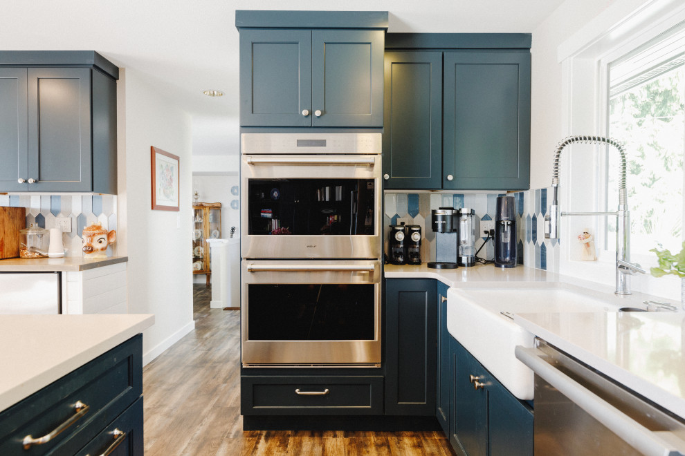 Photo of a mid-sized beach style eat-in kitchen in Seattle with shaker cabinets, blue cabinets, blue splashback, glass tile splashback, dark hardwood floors, with island, brown floor and white benchtop.