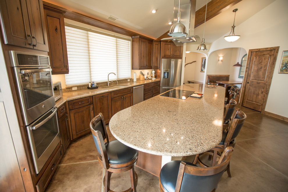 Mid-sized mountain style single-wall concrete floor and gray floor open concept kitchen photo in Denver with an undermount sink, recessed-panel cabinets, dark wood cabinets, granite countertops, beige backsplash, stone slab backsplash, stainless steel appliances and an island