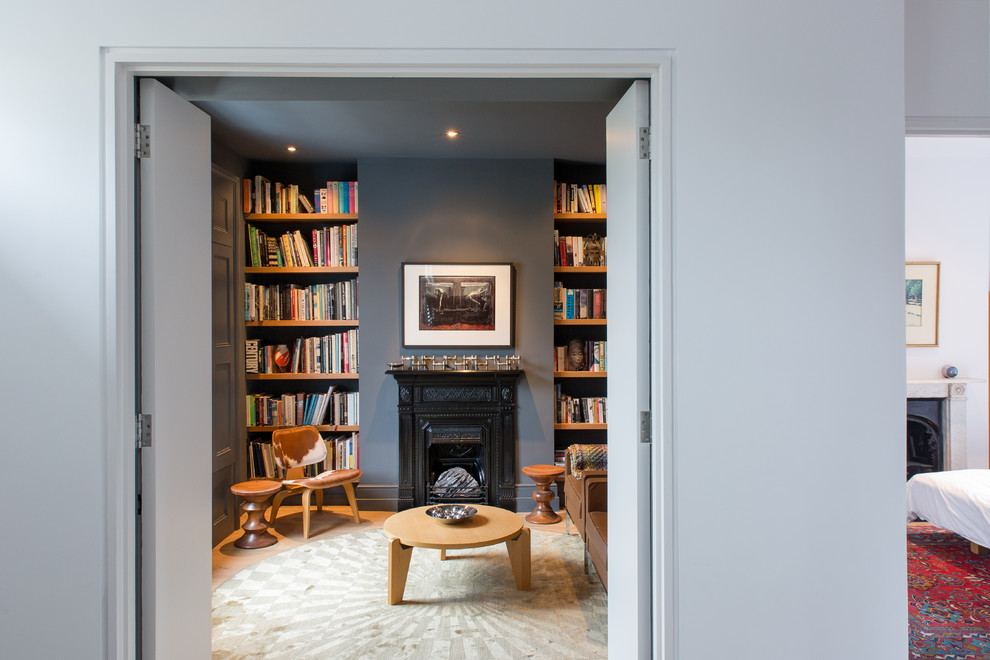 This is an example of a small contemporary enclosed living room in London with a library, blue walls, a standard fireplace and no tv.