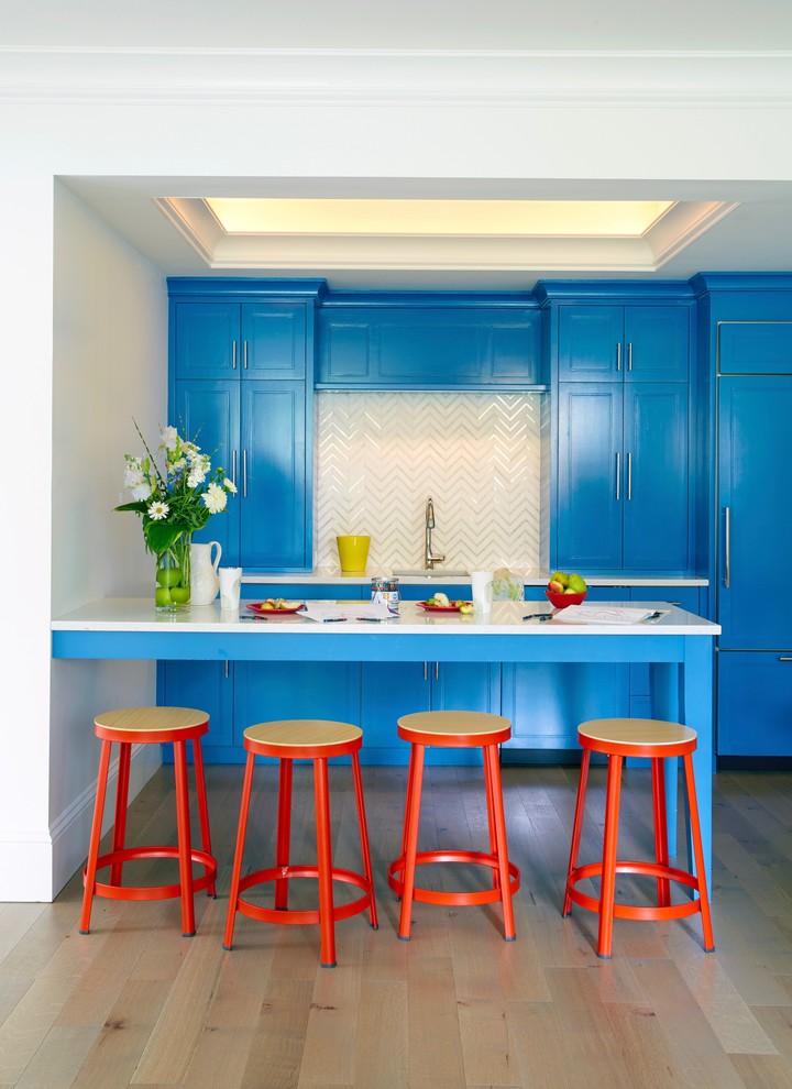 Inspiration for a small beach style kitchen in New York with an undermount sink, recessed-panel cabinets, blue cabinets, quartz benchtops, multi-coloured splashback, panelled appliances, white benchtop, light hardwood floors and a peninsula.